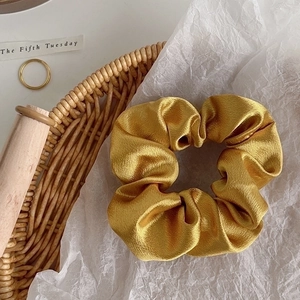 Detailed view of the golden satin hair scrunchie with a glossy texture and soft pleats