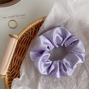 Detailed close-up of a lavender satin scrunchie with silk luster on a rustic basket