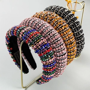 Detail of four colorful rhinestone headbands hanging on a minimalist golden display stand