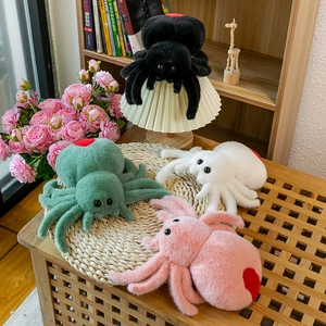 Giant plush spider prank toys in black green pink and white colors on a wooden table