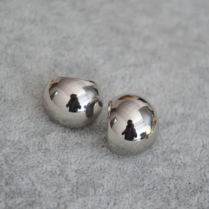 Detailed close-up of large hemispherical silver earrings with high-shine mirror finish