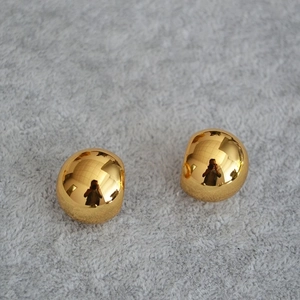 Close-up of polished gold spherical stud earrings on a textured fabric background