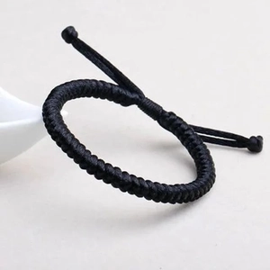 Macro shot of a black hand-woven bracelet with adjustable cord on a gray background