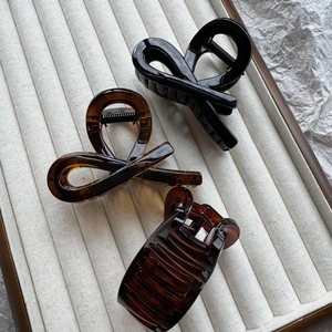 Glossy bow-tie hair claws in black and amber tortoiseshell on a beige display tray