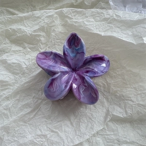 Macro shot of a high-gloss marble-patterned frangipani hair claw in purple tones