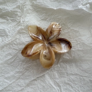 Detail view of flower-shaped hair claw clip with amber marble texture on white background