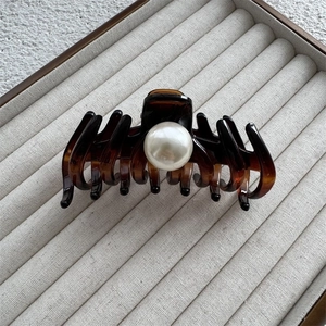 Detail of amber acrylic shark hair claw clip featuring a large pearl on a jewelry tray