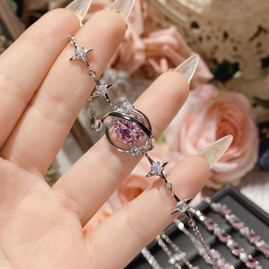 Elegant silver star bracelet with pink gemstone center held by hand against floral background