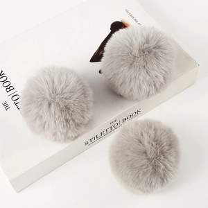 Three light gray faux rabbit fur pom poms for bags and shoes on a white background