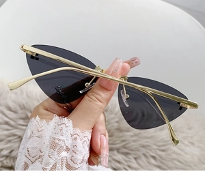 Detail of rimless cat eye sunglasses with gold metal temples and dark gray lenses