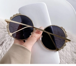 Detailed close-up of round gold metal sunglasses with wavy edges and dark grey lenses
