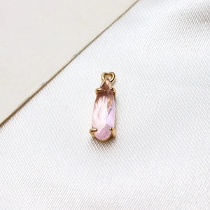 Macro shot of pink teardrop glass pendant in a gold-plated claw setting on silk