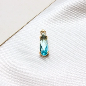 Detail of blue-green teardrop glass pendant with gold-plated claw setting on white silk
