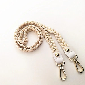 Close-up of woven beige and gold strap with white leather ends and metal lobster clasps
