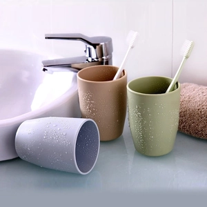 Minimalist plastic toothbrush cups in beige, green, and gray on a wet bathroom counter