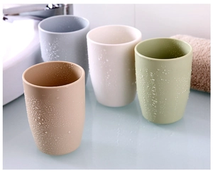 Detail view of four minimalist plastic tooth mugs in neutral tones with fresh water droplets