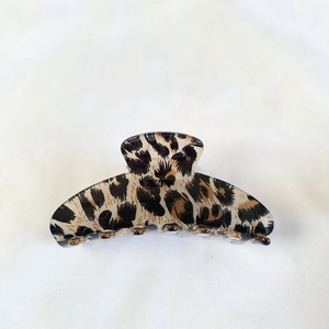 Detail view of a large leopard print hair claw clip on neutral fabric background