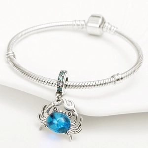 Macro detail of silver crab charm featuring blue crystal and colorful zircon inlays