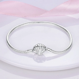 Detail of silver snake chain bracelet featuring a shell-shaped clasp and soft silk fabric