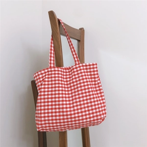 Detail of red and white checkered tote bag hanging on a minimalist wooden chair backrest