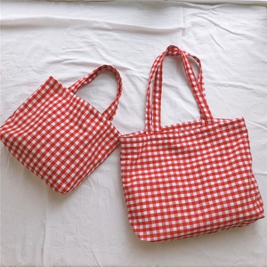 Flat lay of red and white gingham tote bags in two sizes on white textured fabric
