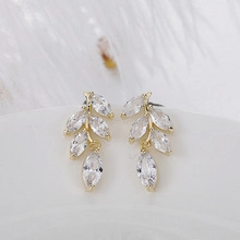Detailed view of gold leaf stud earrings with marquise-cut cubic zirconia on a white plate