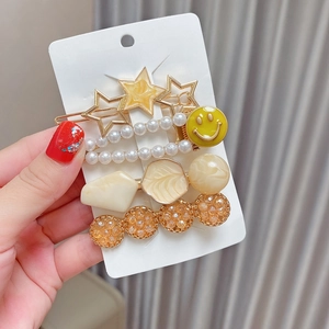 Detail of 5-piece gold hair clip set featuring pearls, stars, and yellow smiley face