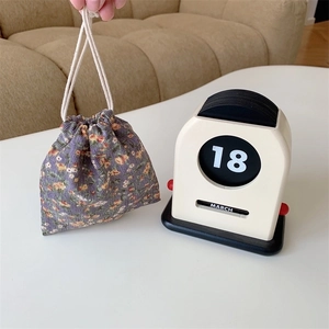 Close-up of a floral drawstring fabric bag held by hand in a cozy home setting