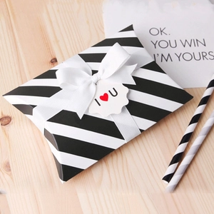 Black and white striped pillow gift box with white ribbon and heart tag on wood