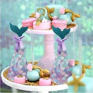 Mermaid party favor boxes with sparkling glitter fishtail and purple ribbon on a dessert stand