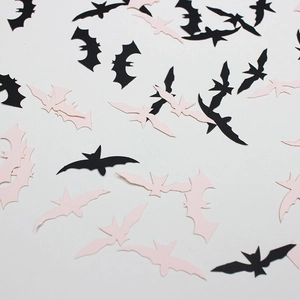 Halloween party confetti with black and light pink paper bat shapes on white background