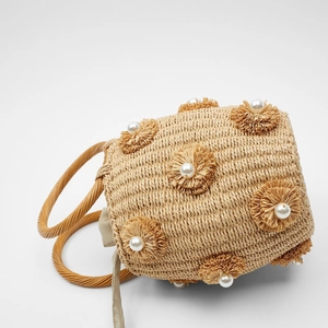 Close-up of woven straw bucket bag featuring pearl-centered floral accents and lining
