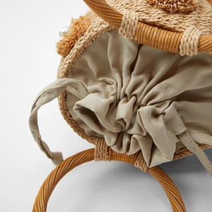Detail view of woven straw bag featuring pearl decor, pom poms and drawstring closure