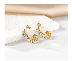 Macro detail of gold-plated C-shaped hoop earrings featuring sparkling zircon stone pavé