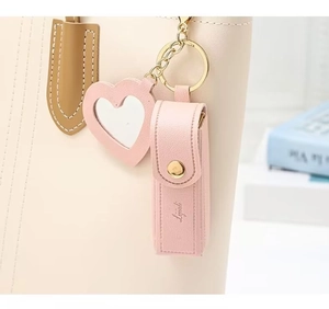 Pink faux leather lipstick pouch with heart mirror charm attached to a beige handbag