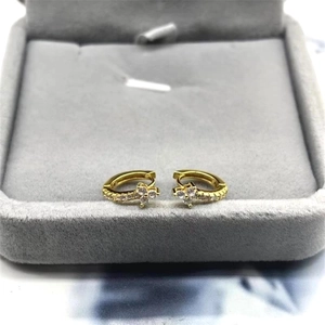 Detailed close-up of golden hoop earrings with white zircon flower pendants on jewelry box
