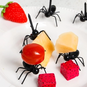 Creative black ant-shaped food picks shown piercing fresh fruit on a white plate