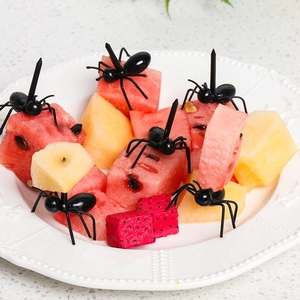 Macro shot of black ant-shaped plastic fruit forks holding pieces of fresh fruit on a plate