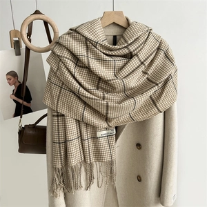 Detail of khaki houndstooth scarf with tassels draped over a beige trench coat