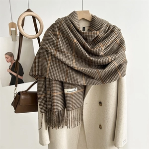 Detail of a brown houndstooth scarf with fringe and a white woven label on a beige coat