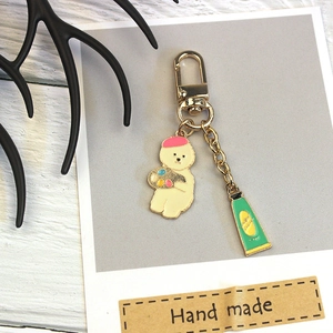 Creative alloy bichon dog keychain with pink beret and paint tube charms on white wood background