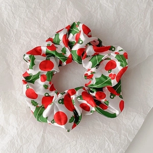 Detailed top view of a white satin Christmas scrunchie with holly and red ball prints