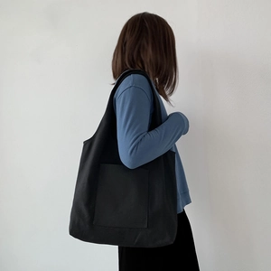 Minimalist black canvas tote bag with front pocket shown on shoulder by a model