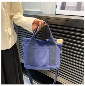 Blue canvas tote bag with dual handles and adjustable strap shown on person