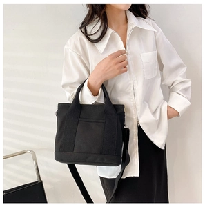 Detail of a minimalist black canvas tote bag showing the handles and removable shoulder strap