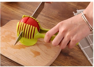 Close-up of a green handheld slicer tool for even tomato and lemon slices on wood