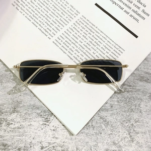 Macro shot of rectangular metal sunglasses with gold frames and dark lenses on a grey texture