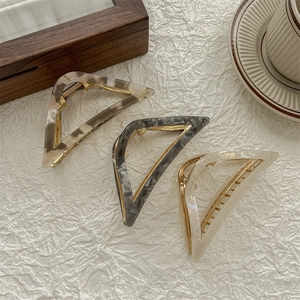Three acetate triangle hair claws in amber, marble, and pearl white with gold frames