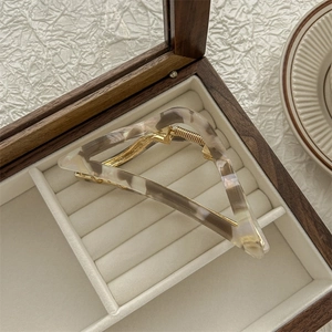 Detail of triangular marble acetate hair claw clip resting in a velvet lined wooden box