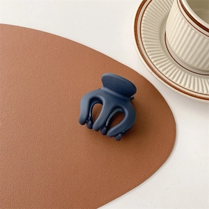 Detail of matte navy blue hair claw clip on leather mat with stylish coffee cup background